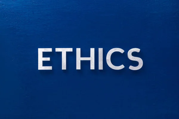 The word ethics laid with silver metal letters on classic blue board in flat lay with central composition — 스톡 사진