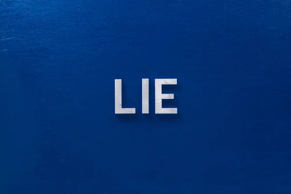 The word lies laid with silver metal letters on classic blue board in flat lay with central composition — 스톡 사진