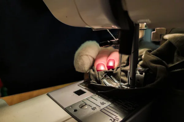 A hand of aged womans with a bandaged finger sews with a sewing machine — Stock Photo, Image