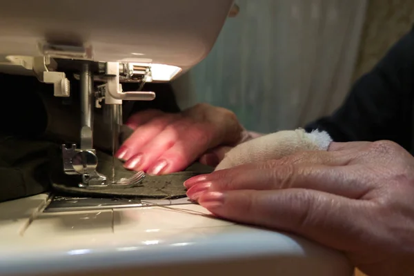 A hand of aged womans with a bandaged finger sews with a sewing machine — Stock Photo, Image