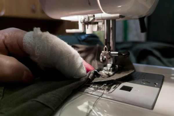 A hand of aged womans with a bandaged finger sews with a sewing machine — 스톡 사진