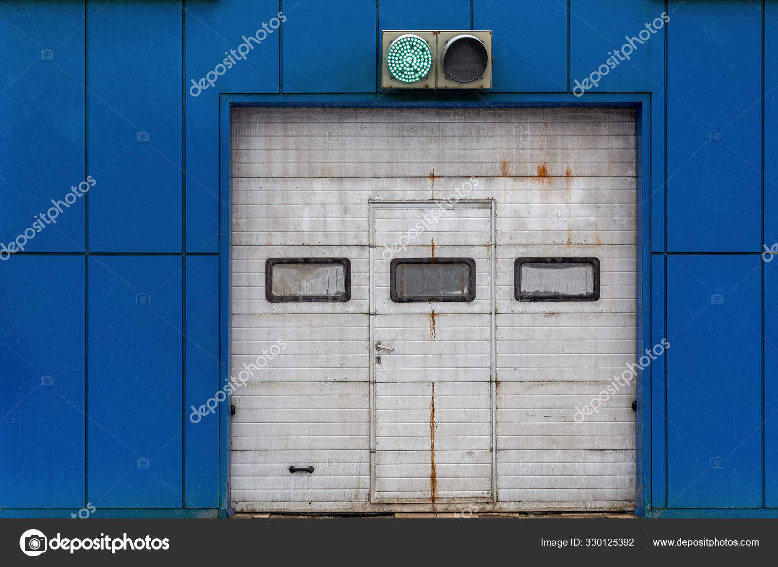 A White Automatic Upward Sliding Gate On Blue Garage With Green