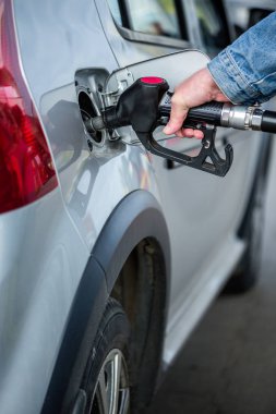 Benzin istasyonunda yakıt ikmali yapan kot ceketli gri metalik araba - seçici odaklı yakın plan - dikey bileşim