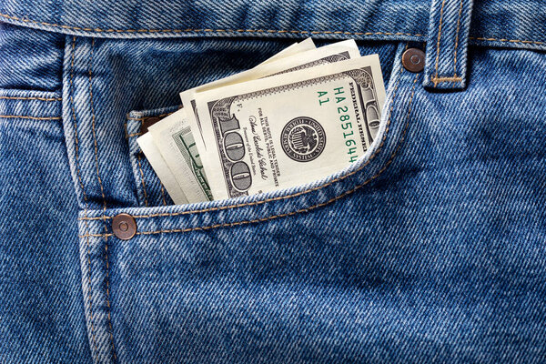 US dollar banknotes in the front left pocket of blue jeans. Concept of saving money or pocket expenses