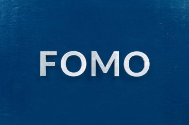 Fomo kelimesinin kısaltması - kaçırılma korkusu - klasik mavi düz yüzey üzerine gümüş harflerle yazılmıştır.