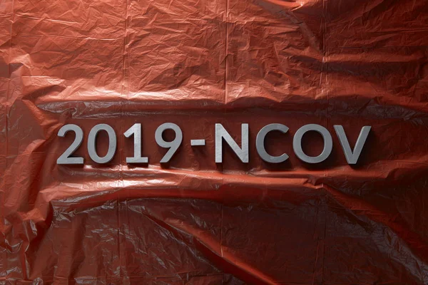 Слово 2019-NCOV уложено металлическими буквами на скомканном красном пластиковом фоне в плоской композиции — стоковое фото