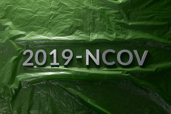 Слово 2019-NCOV укладывается металлическими буквами на зеленом смятом полиэтиленовом фоне пленки в плоской композиции — стоковое фото