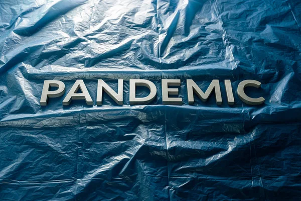 The word pandemic laid with silver letters on crumpled blue plastic film background. Slanted perspective. — Stock Photo, Image