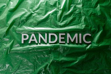the word pandemic laid with silver letters on green crumpled plastic film background in flat lay composition at center