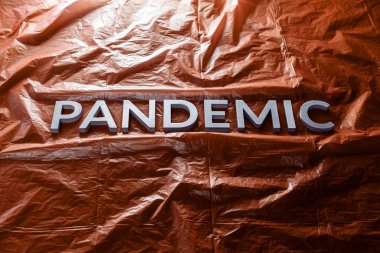 The word pandemic laid with silver letters on red crumpled plastic film background. Slanted perspective.