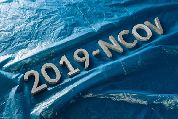 Слово 2019-NCOV укладывается металлическими буквами на смятом классическом синем пластиковом фоне в наклонной диагональной композиции — стоковое фото
