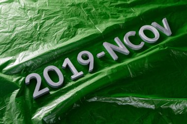 The word 2019-NCOV laid with metal letters on green crumpled plastic film background in slanted diagonal composition