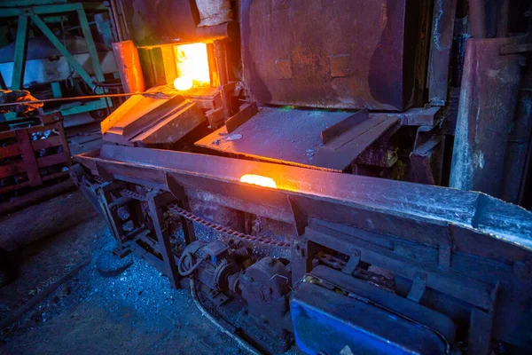 Un proceso de mover la pieza de trabajo luminosa de acero caliente del horno al martillo con el transportador de cadena . —  Fotos de Stock