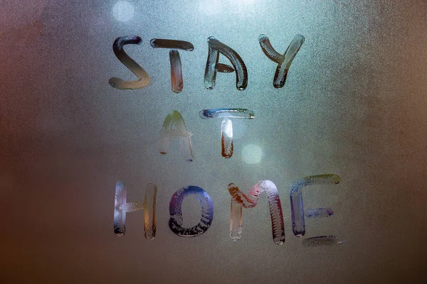 the words stay at home handwritten on wet window glass at night - close-up full frame picture with selective focus