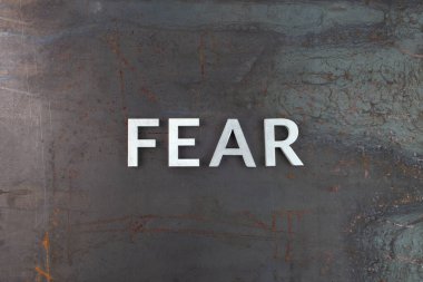 Ham paslı çelik yüzeye gümüş harflerle yazılmış korku sözcüğü, kompozisyonun hemen üstünde düz bir şekilde yatıyordu.