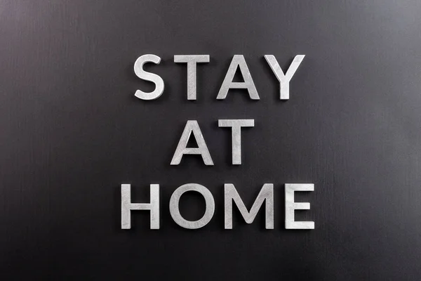 Слова "остаться дома", выложенные серебряными металлическими буквами на матовом черном фоне в плоской светлой перспективе; — стоковое фото