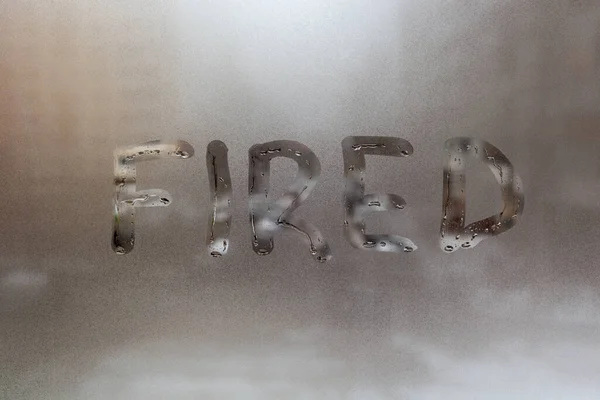 the word fired handritten on wet window glass at cloudy weather