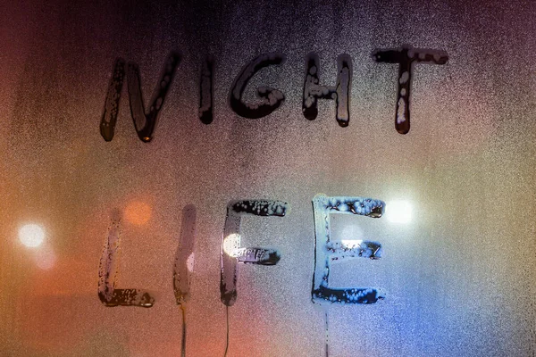 夜のぬれた窓ガラスの表面に手書きの単語の夜の生活 選択的な焦点と背景のぼかしでクローズアップ — ストック写真