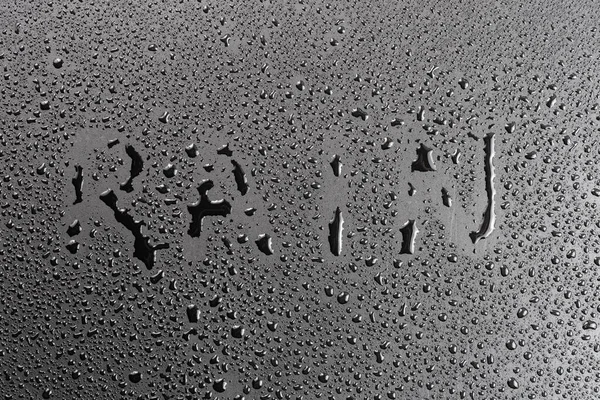 the word rain handwritten on matte black hydrophobic matte surface with water drops.