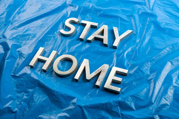 Слова "остаться дома", выложенные серебряными металлическими буквами на потрепанном синем пластиковом фоне в косых тонах; — стоковое фото