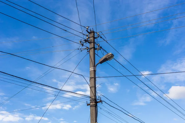 Concrete lamp post with many cables connected radially on blue sky with feather clouds in the background, Centered composition. — Stock Photo, Image