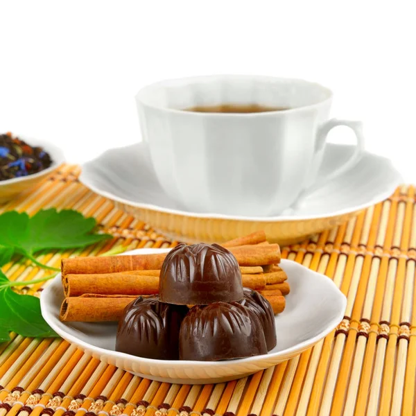 Taza de té, chocolates y canela en estera de bambú sobre blanco —  Fotos de Stock