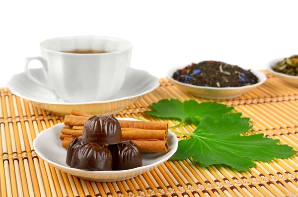 Tea cup, chocolates and cinnamon on bamboo mat on white — Stock Photo, Image