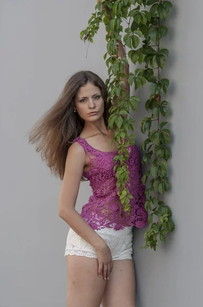 Hermosa chica de pelo largo en la parte superior transparente y está posando contra una pared —  Fotos de Stock