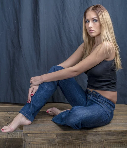 Young slender blonde girl in jeans and shirt posing coquettishly — Stock Photo, Image