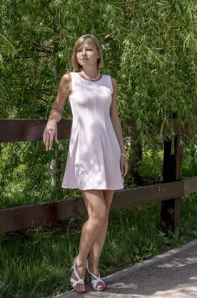 Mujer rubia joven de pie en el árbol del jardín en la primavera —  Fotos de Stock