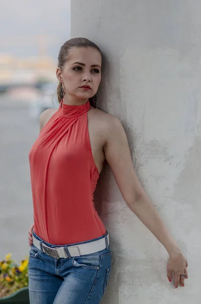 Giovane bella ragazza bionda in una camicetta estiva rossa e jeans in posa flessibile — Foto Stock