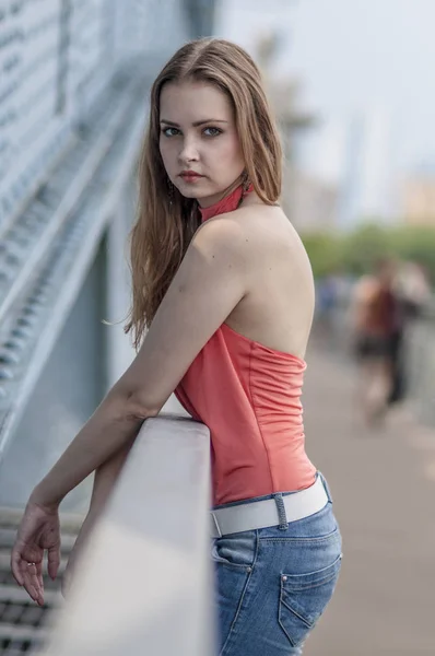 Junge schöne blonde Mädchen in einer roten Sommerbluse und Jeans posiert flexibel — Stockfoto