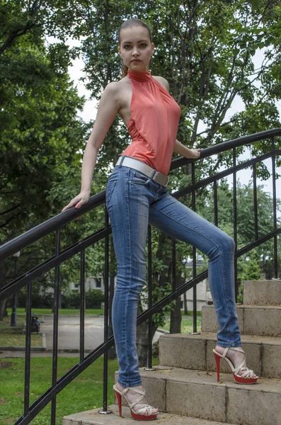 Ung vacker blond tjej i en röd sommar blus och jeans poserar flexibla — Stockfoto