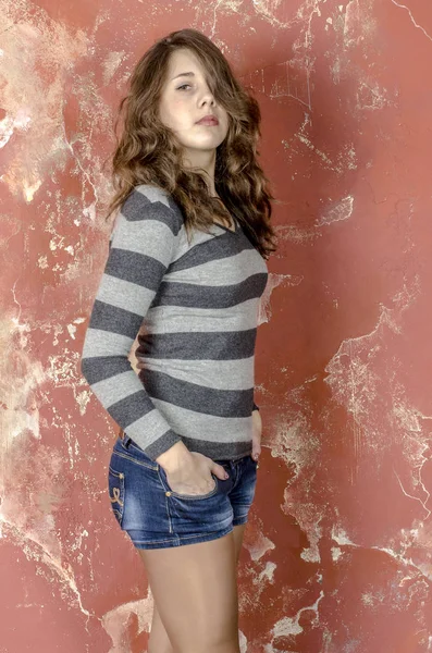 Молодая веселая девушка в джинсовых шортах и в полосатом свитере ходит в юном стиле — стоковое фото