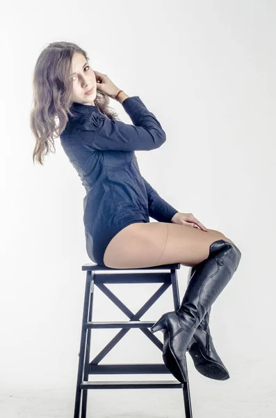 Молодая девушка с вьющимися волосами сидит изящно кокетливая в темной рубашке и высоких сапогах на каблуках — стоковое фото