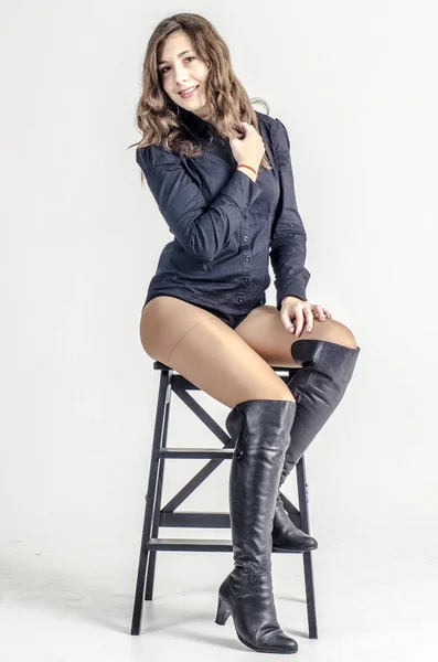 Young girl with curly hair sits gracefully coquettish in a dark shirt and high boots with heels — Stock Photo, Image