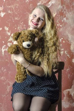 Bir benekli kıvırcık uzun saçlı genç sarışın kız elbise oyuncak ayı ile