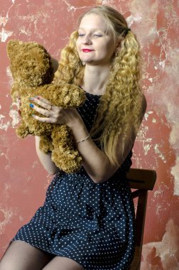 Bir benekli kıvırcık uzun saçlı genç sarışın kız elbise oyuncak ayı ile