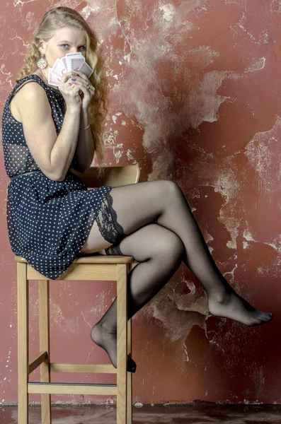 Gadis muda berambut keriting pirang dengan gaun panjang dengan titik-titik polka dan kaus kaki dengan bermain kartu — Stok Foto