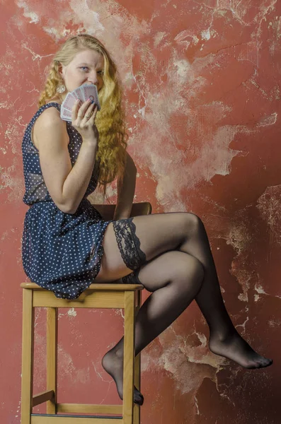 Young girl with blonde curly hair in a long dress with polka dots and stockings with playing cards — Stock Photo, Image