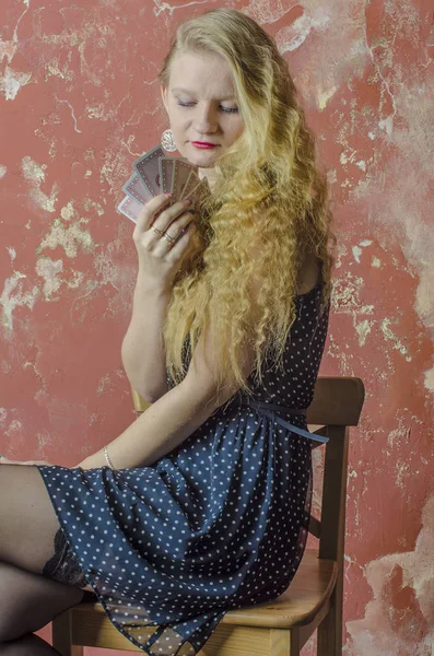 Gadis muda berambut keriting pirang dengan gaun panjang dengan titik-titik polka dan kaus kaki dengan bermain kartu — Stok Foto