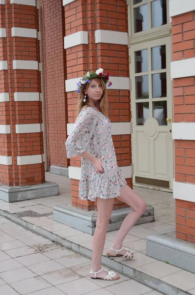 Ένα κορίτσι με μακριά μαλλιά με ένα στεφάνι από λουλούδια και ένα φόρεμα του καλοκαιριού — Φωτογραφία Αρχείου