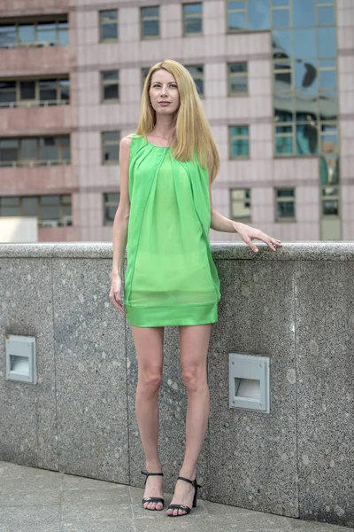 市内の路上で緑の短い夏で美しいブロンドの女の子のドレスします。 — ストック写真
