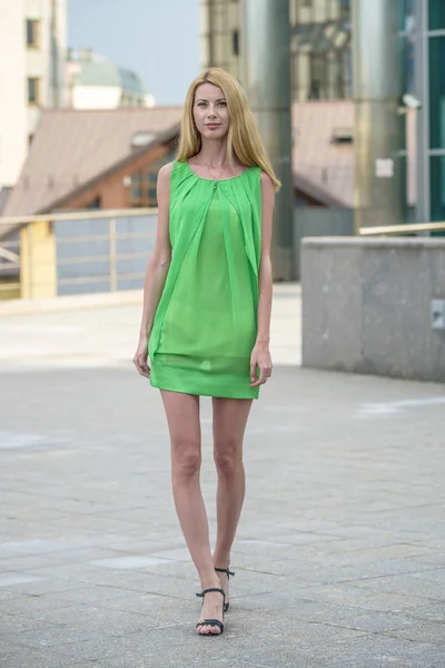 Beautiful blonde girl in a green short summer dress on the streets of the city — Stock Photo, Image