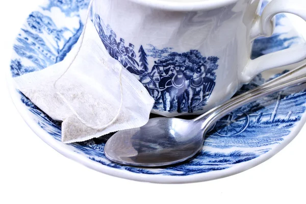 Macro shot of a tea bag and spoon on a decorative cup and plate — Stock Photo, Image
