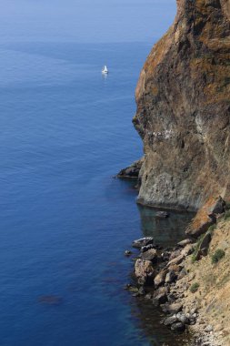 Mavi deniz ve büyük bir dağ kayalık kıyıya yakın küçük bir beyaz yelkenli