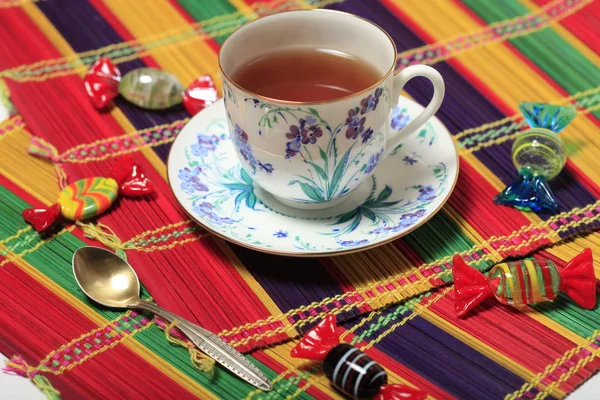 Thé dans une belle tasse avec un motif de fleurs et des bonbons sur une serviette en bambou — Photo