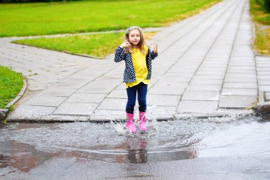 Mutlu sevimli küçük kız su birikintisine yaz aylarında yağmur sonrası atlama