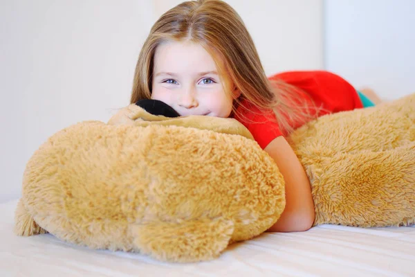 Doce menina está abraçando um ursinho de pelúcia enquanto deitado em sua cama — Fotografia de Stock