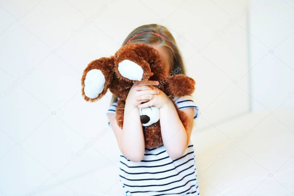 Little scared kid hiding behind teddy bear